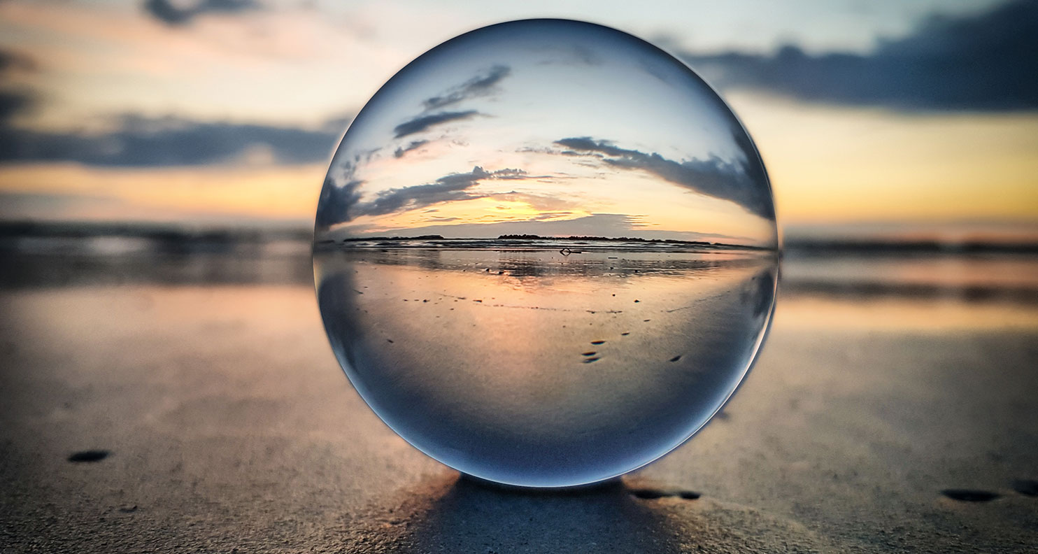 Glass sphere sitting in sand on a beach.